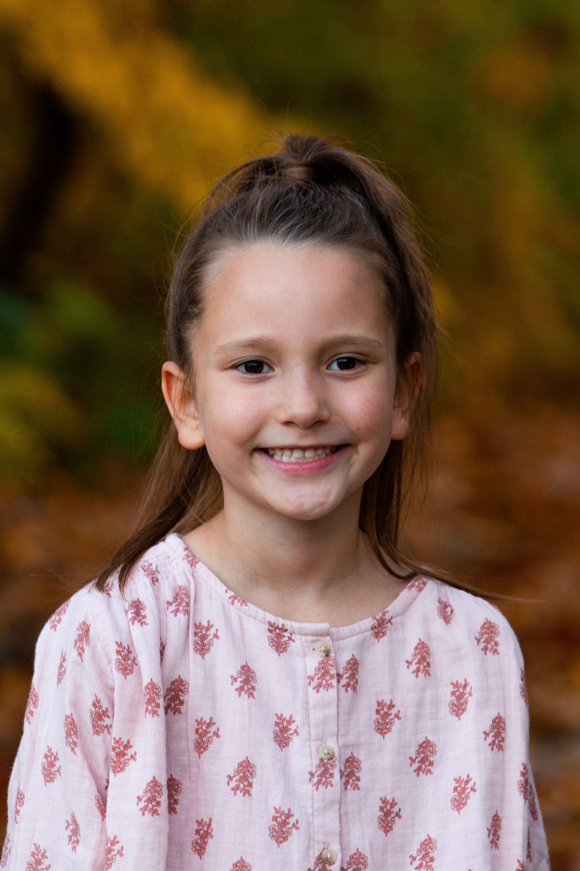 A young girl in a pink shirt is smiling for the camera.