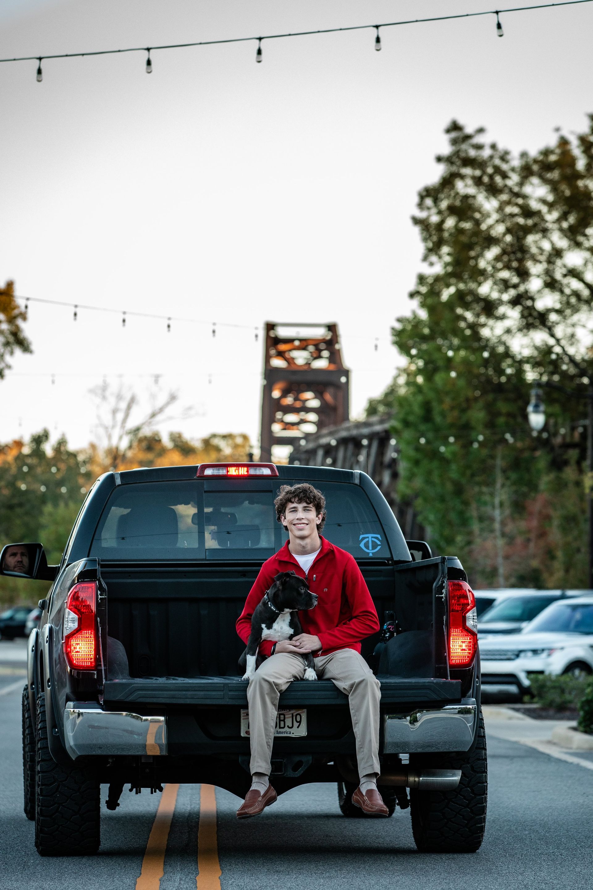 A man is sitting on the back of a truck holding a dog.