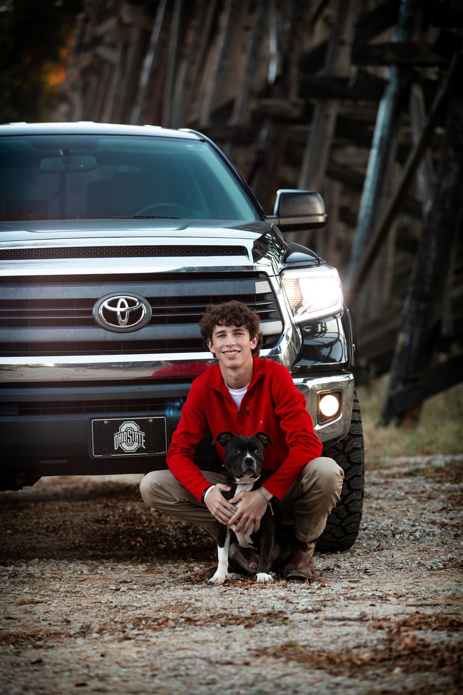A young man is kneeling down next to a truck with a dog.