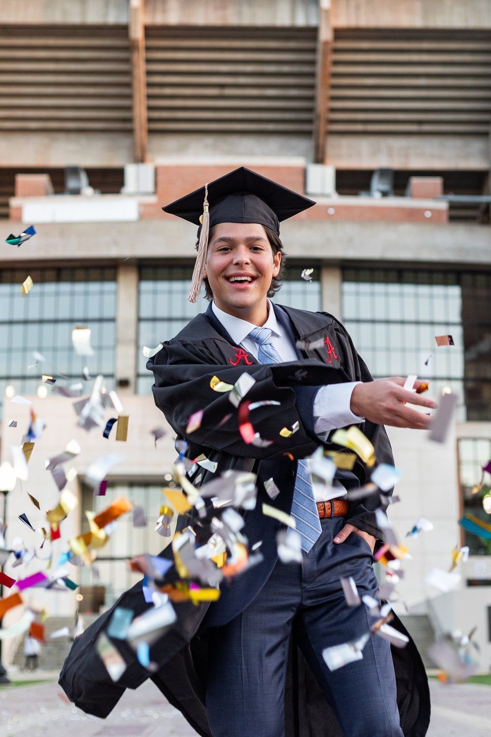A man in a graduation cap and gown is throwing confetti in the air.