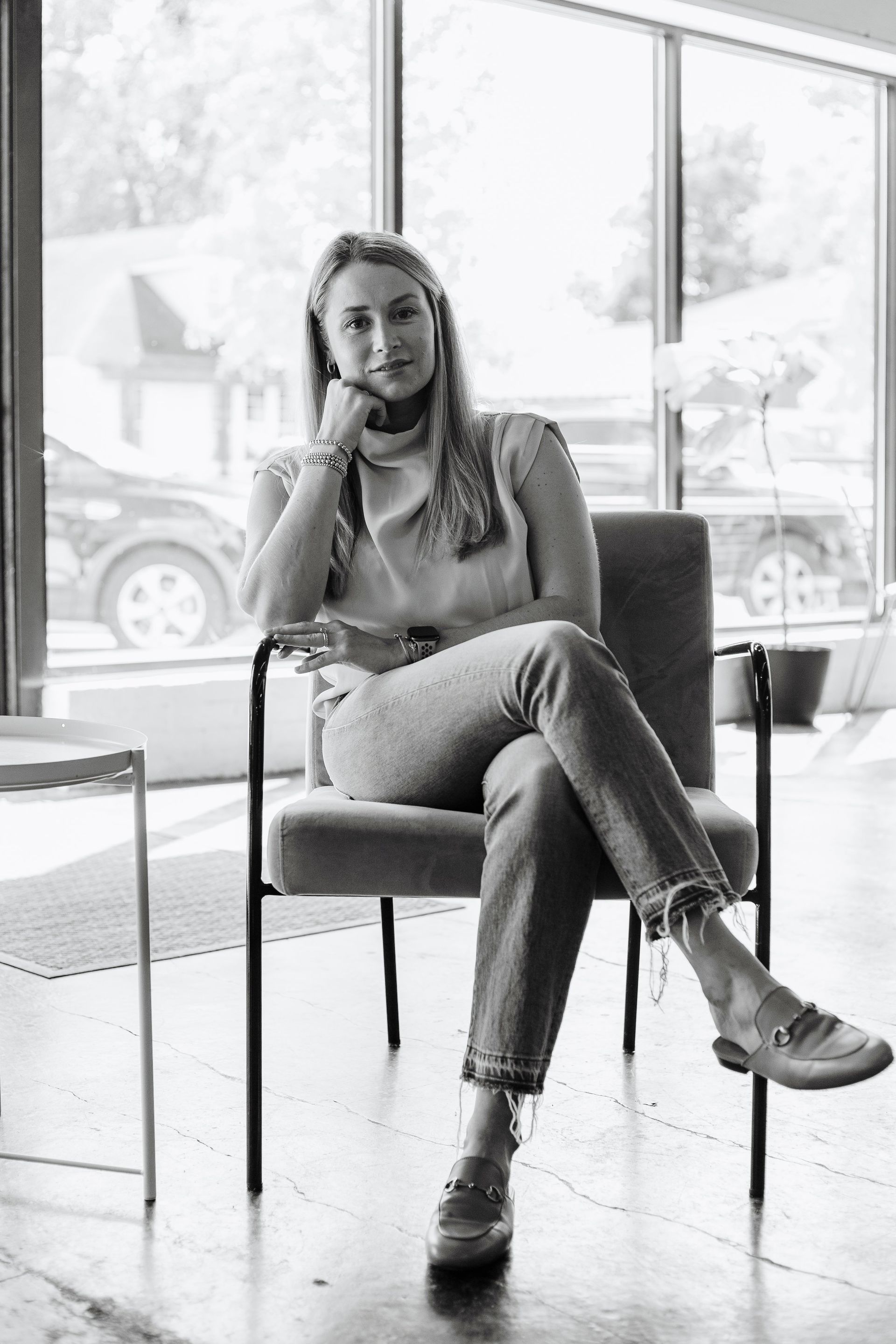 A woman is sitting in a chair in front of a window in a black and white photo.