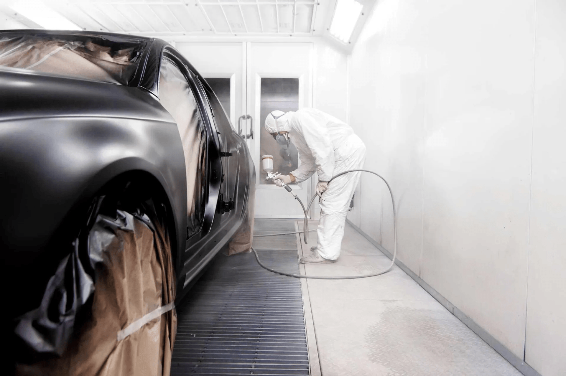 A man is painting a car in a paint booth.