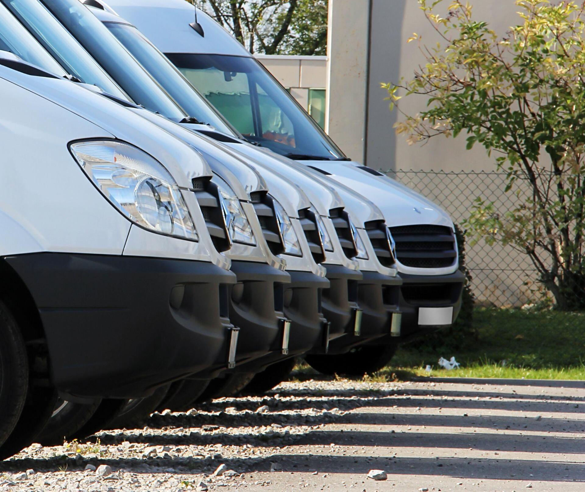 A row of white vans are parked next to each other