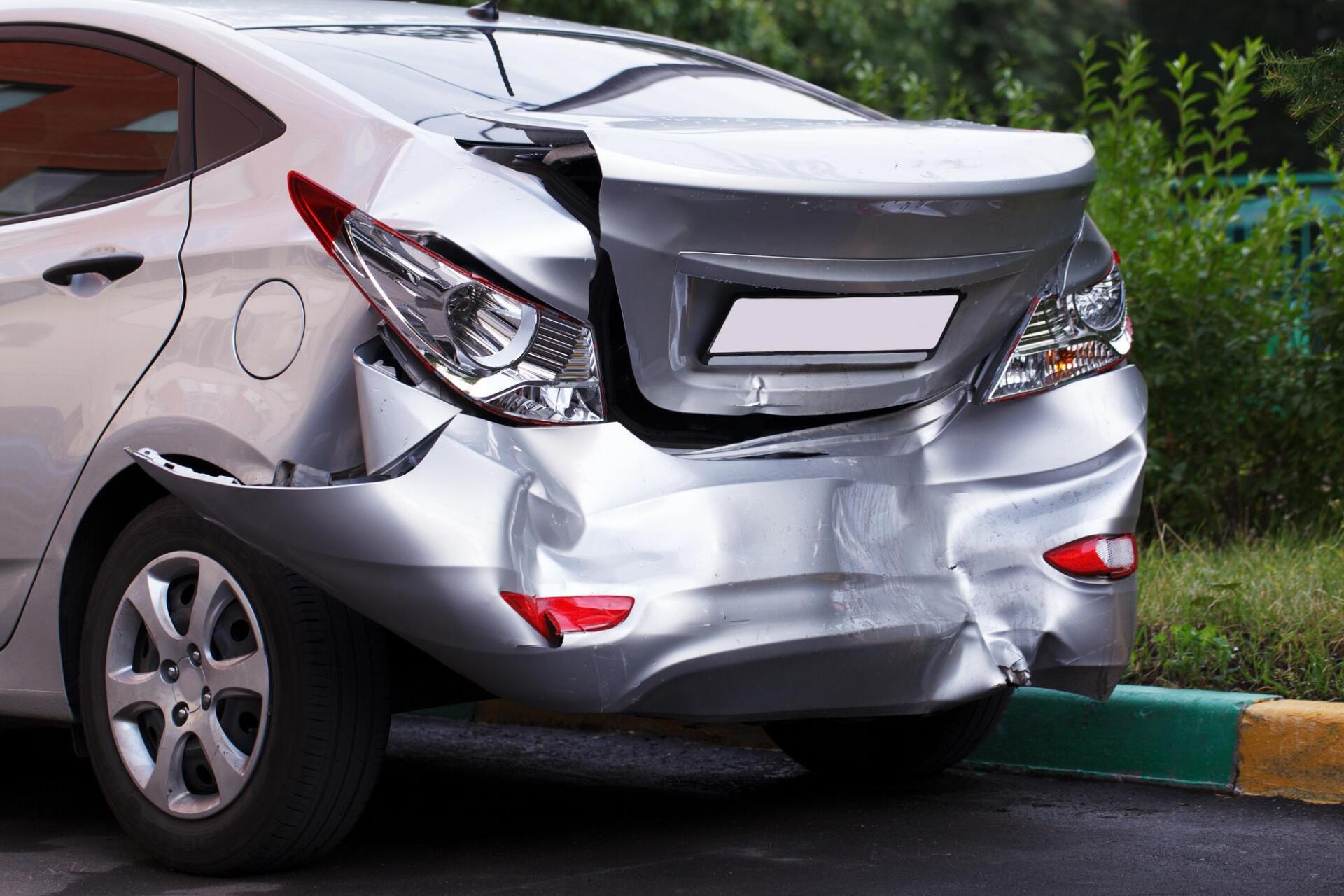 A silver car with a damaged rear end is parked on the side of the road.