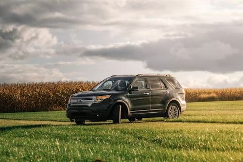 Black SUV parked in a grassy field under a cloudy sky, with a cornfield in the background