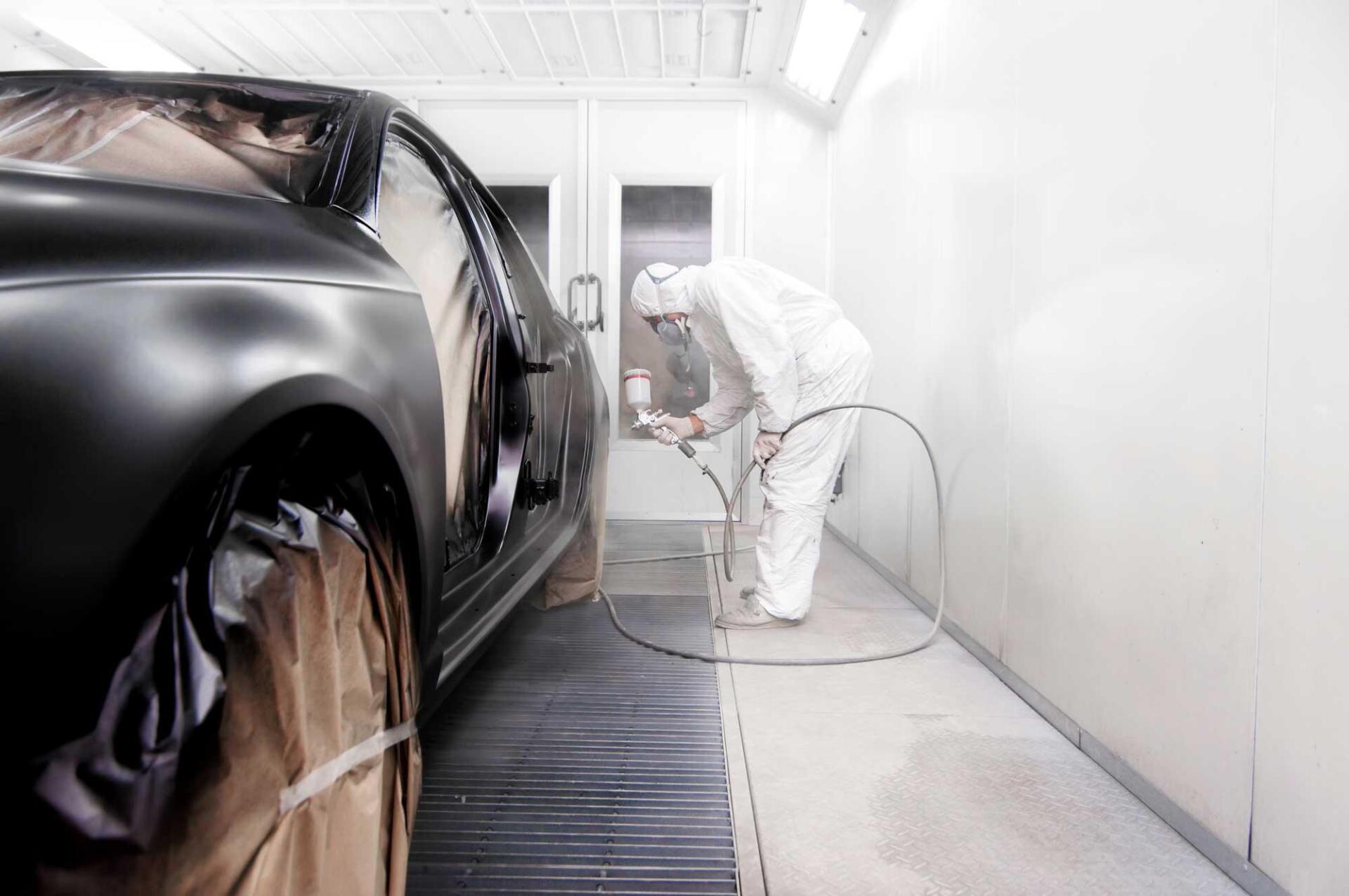 A man is painting a car in a paint booth.