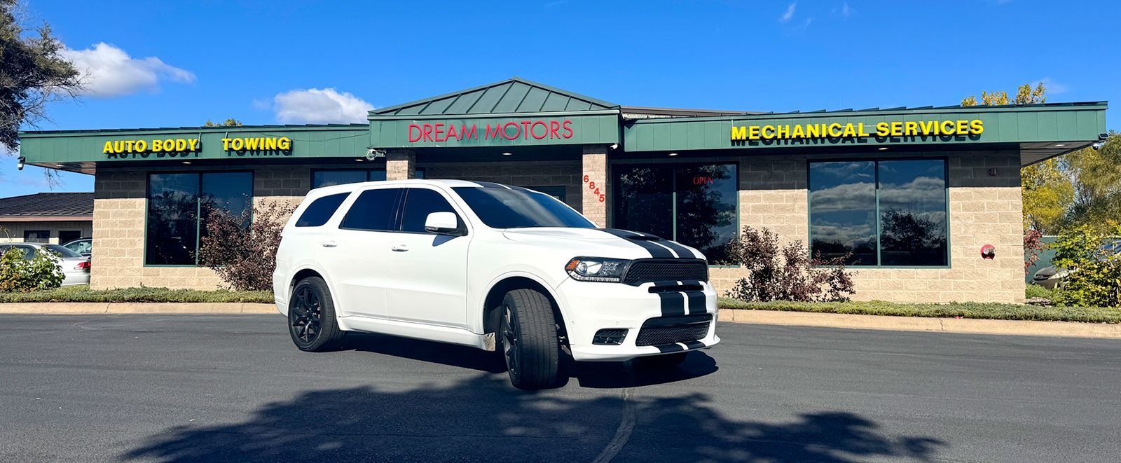 A white dodge durango is parked in front of a dream motors building.