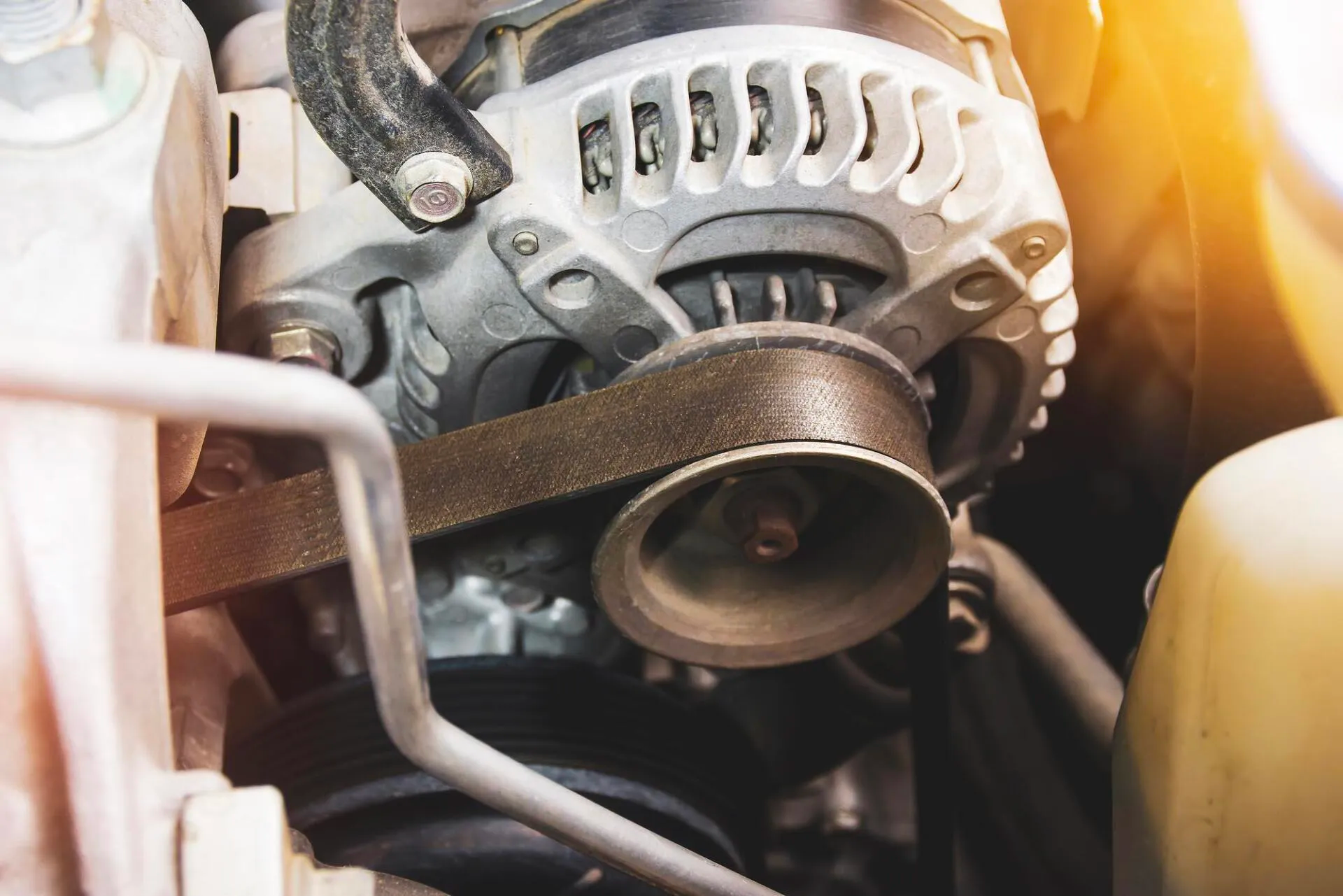 A close up of an alternator and belt on a car engine.