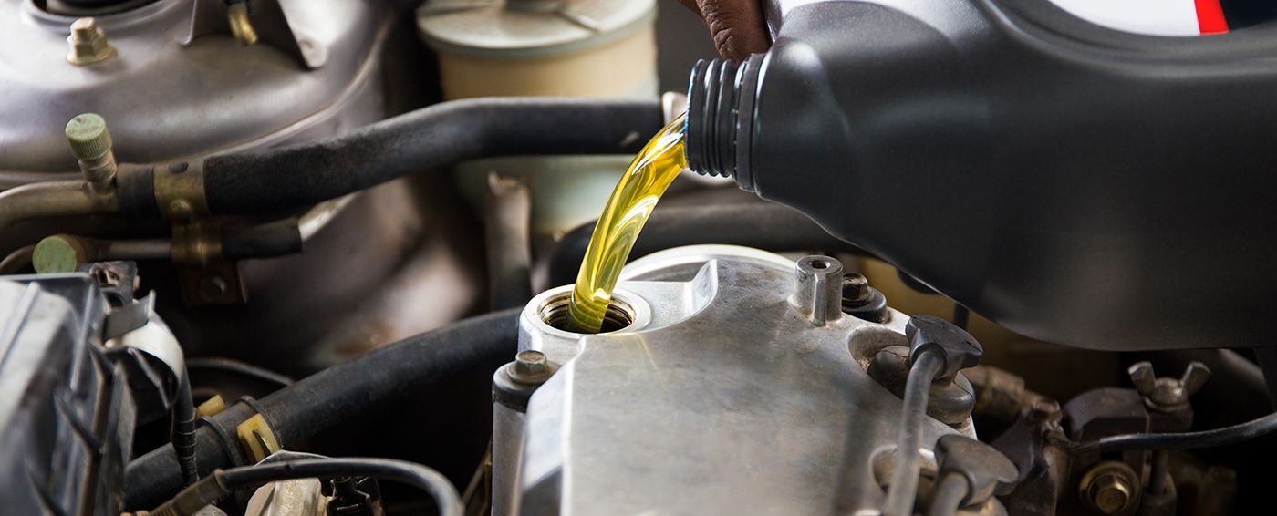 Pouring yellow oil into an engine's oil fill tube from a black container.