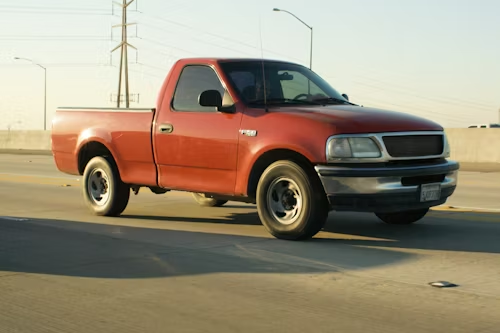 Red Ford pickup truck driving on a road.