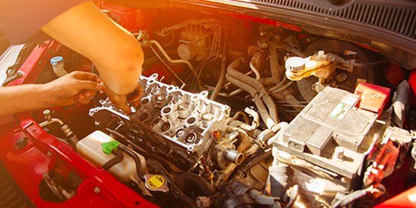A person is working on the engine of a red car.