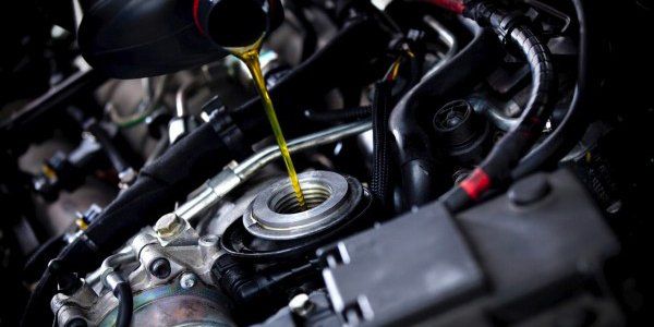 A close up of a person pouring oil into a car engine.