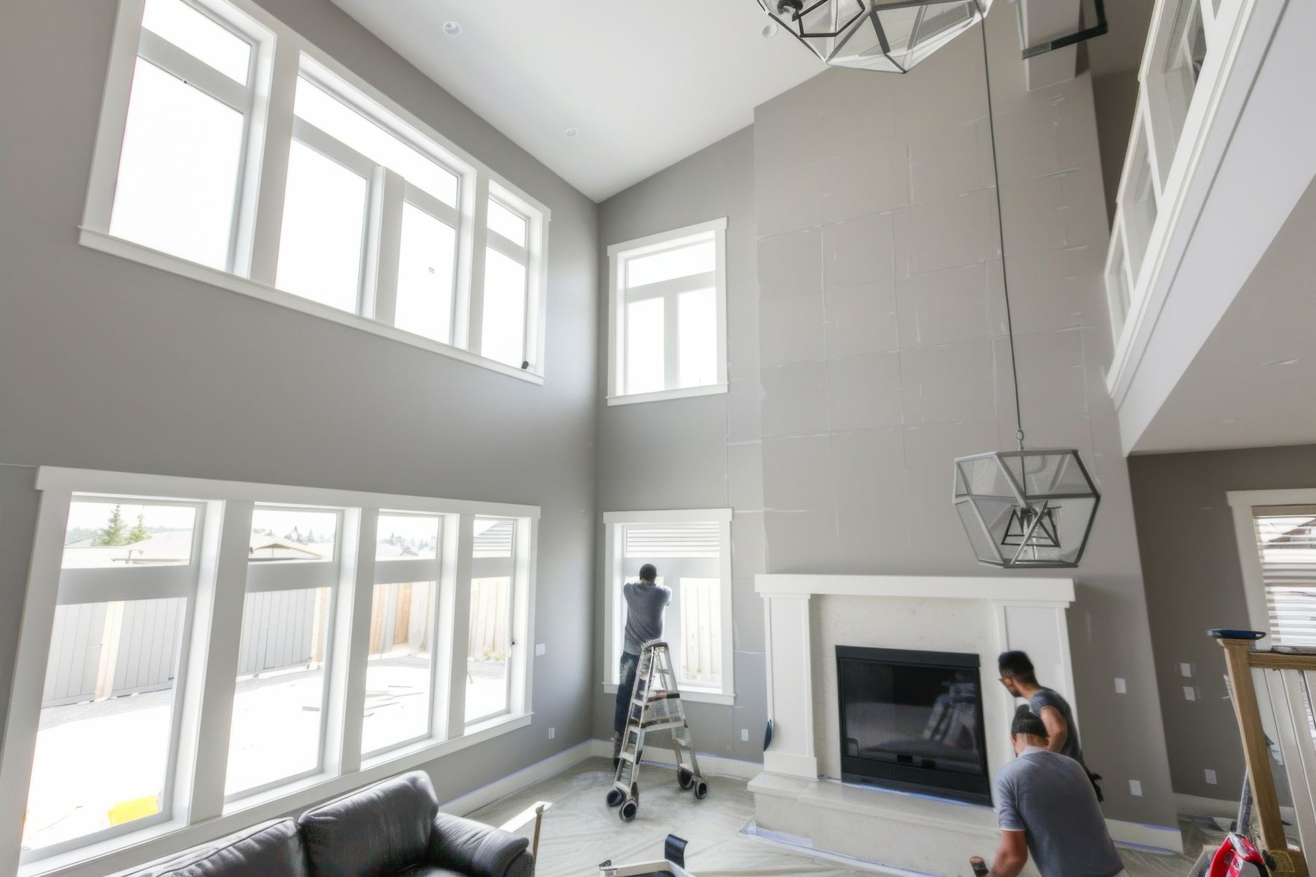 Bright living room with tall windows, fireplace, and two people working near a ladder