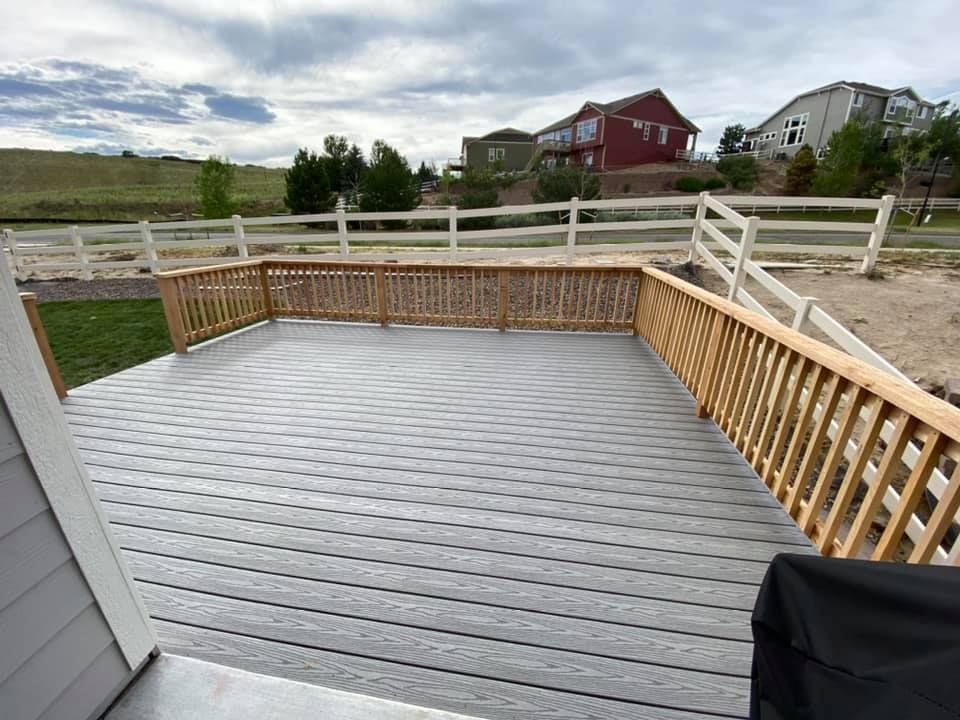 A large gray deck with a wooden railing and a white fence.