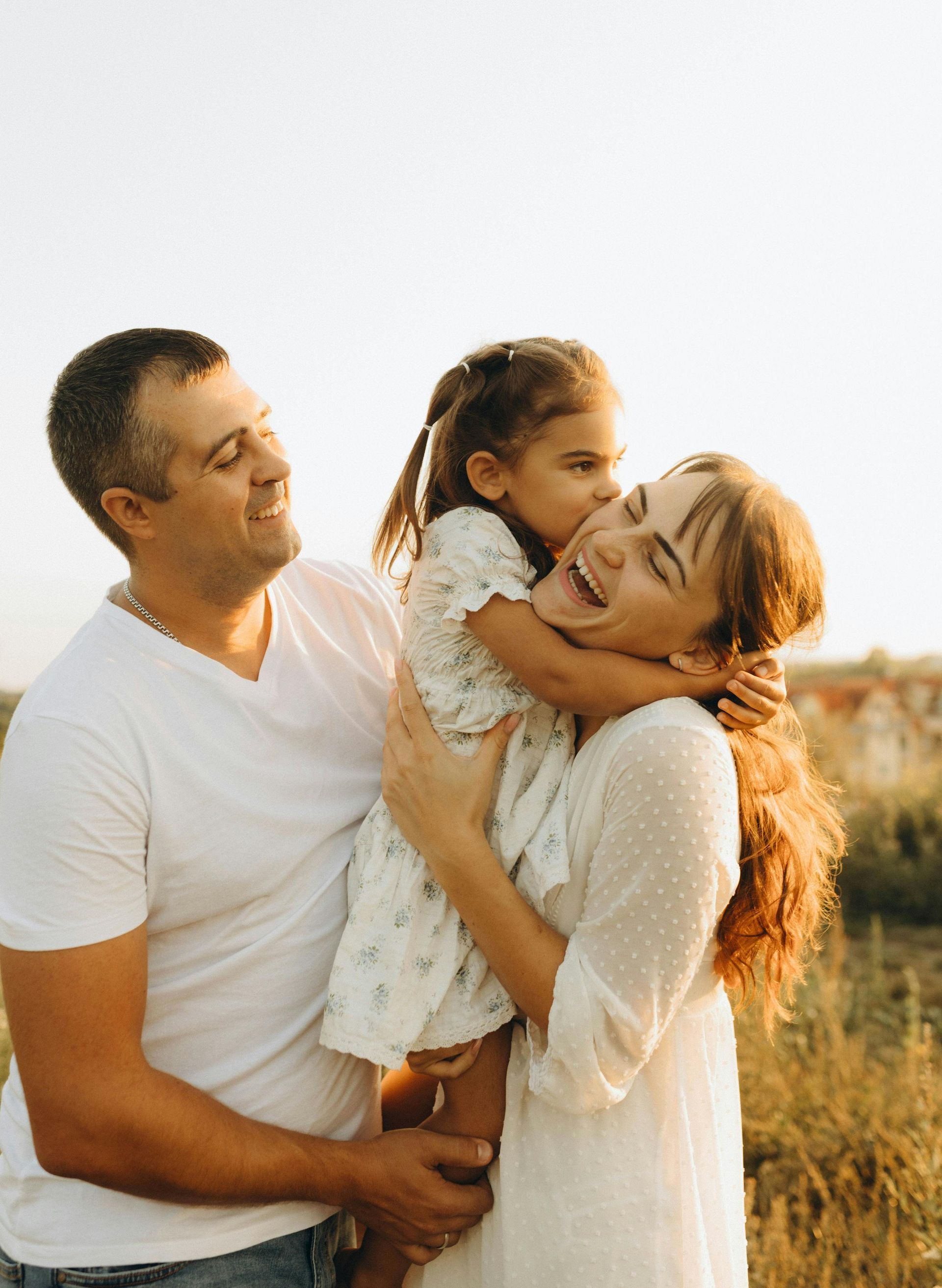 Family in a sunlit field, smiling and hugging a young child.