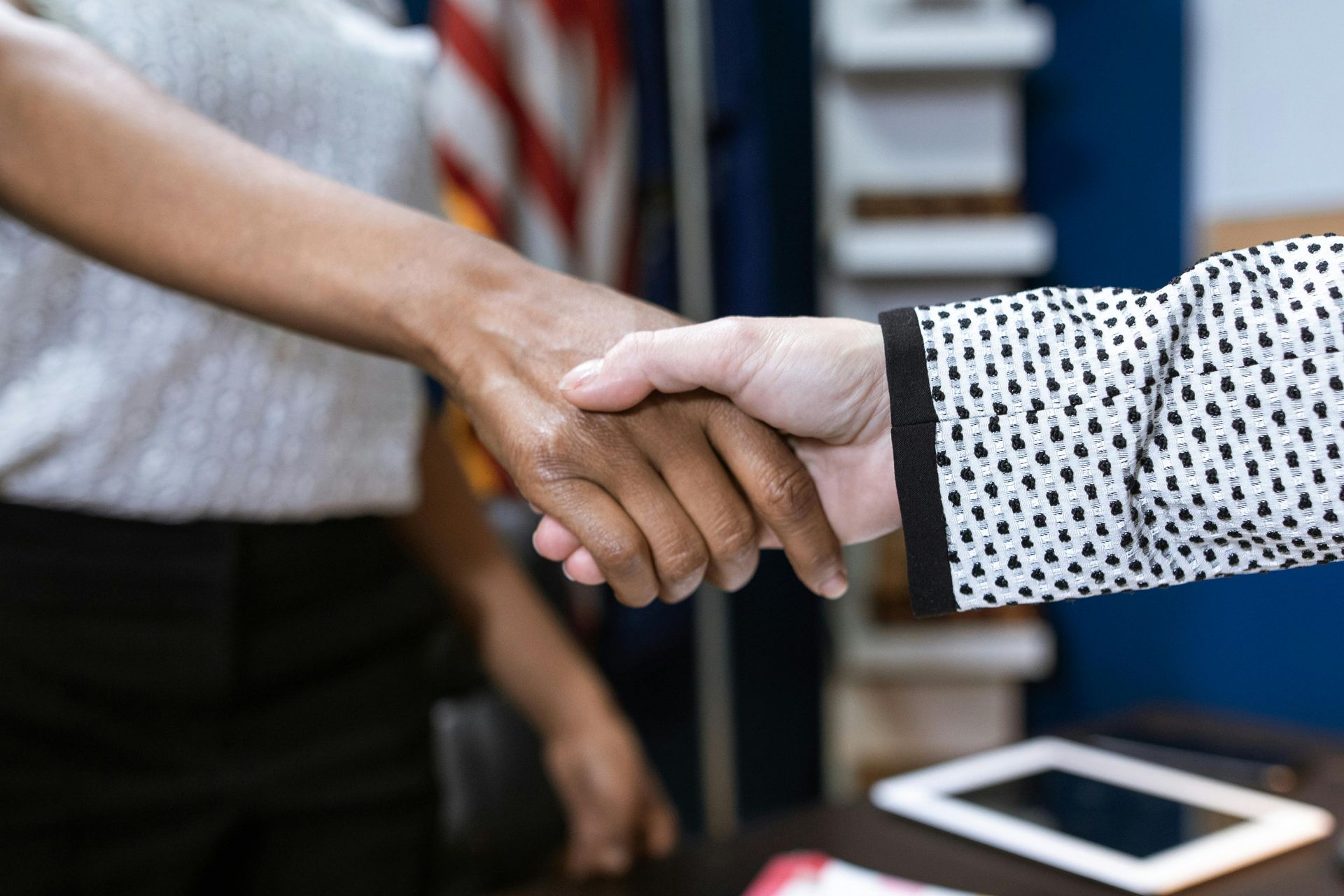 Two people shaking hands across a table with a tablet in the foreground