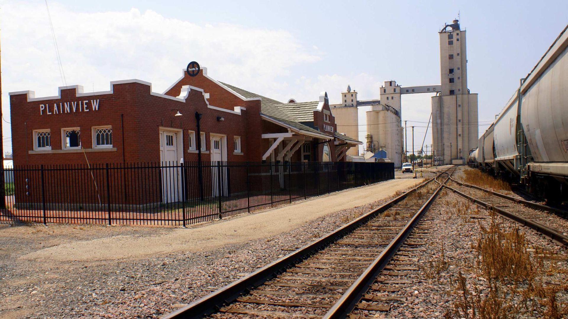 Railroad tracks beside a red brick building and grain silos under a clear sky