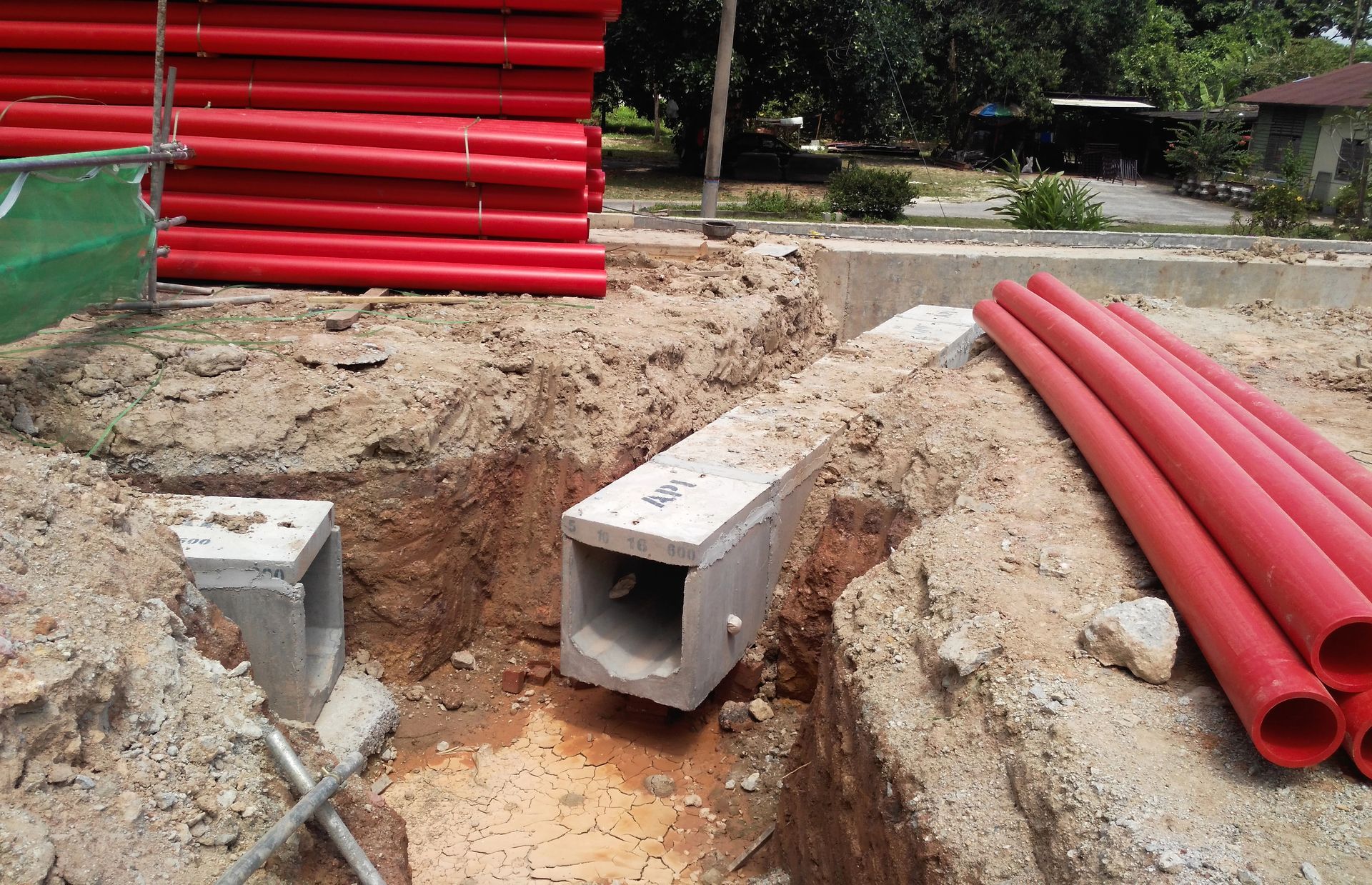 Cantiere edile con tubi rossi, scatole di derivazione in cemento e trincea scavata nel terreno.
