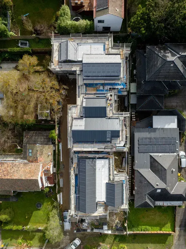 Aerial view of buildings under construction with flat dark gray roofs and solar panels.