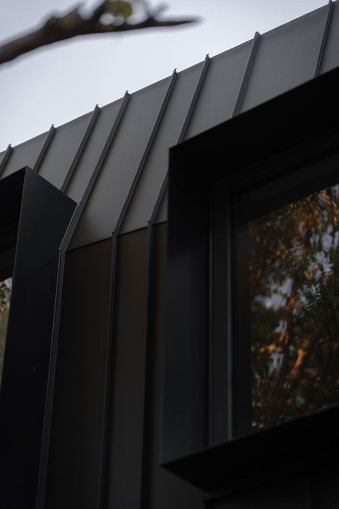 Modern building exterior with dark gray metal siding and angled roof, black window frames.