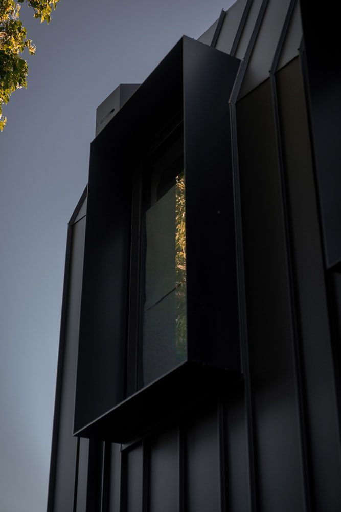 Black, angular building with a rectangular window frame reflecting golden light, against a gray sky.