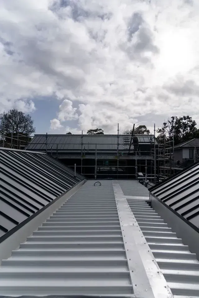 A new white corrugated metal roof with scaffolding in the background under a cloudy sky.