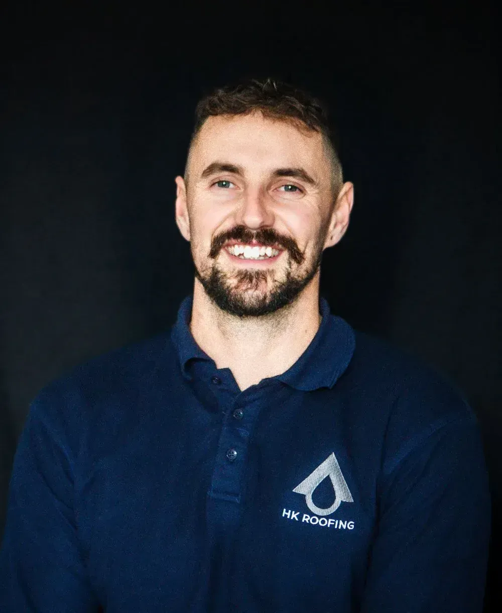 Man in blue shirt, smiling, with logo, against a black background.