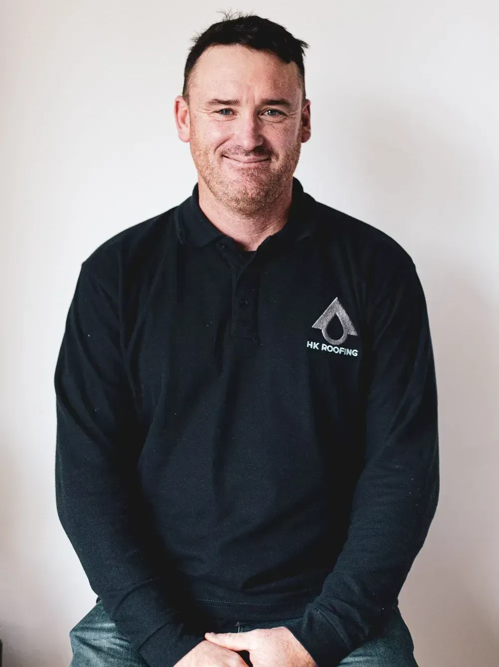 Man wearing dark blue shirt with logo, smiling, indoors.