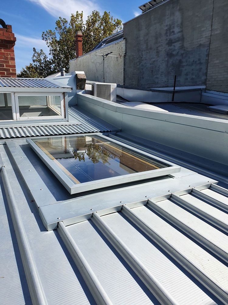 Rooftop with white corrugated metal roofing, skylights, and a brick wall beside concrete walls