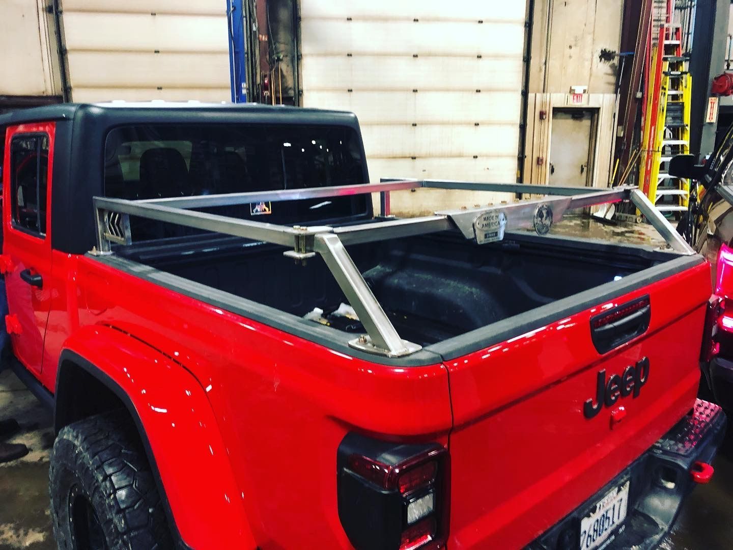 A red Jeep Gladiator pickup truck parked in a garage with a metal utility rack installed over its cargo bed.