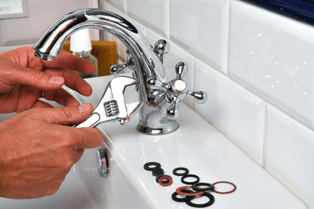 A person is fixing a sink faucet with a wrench.