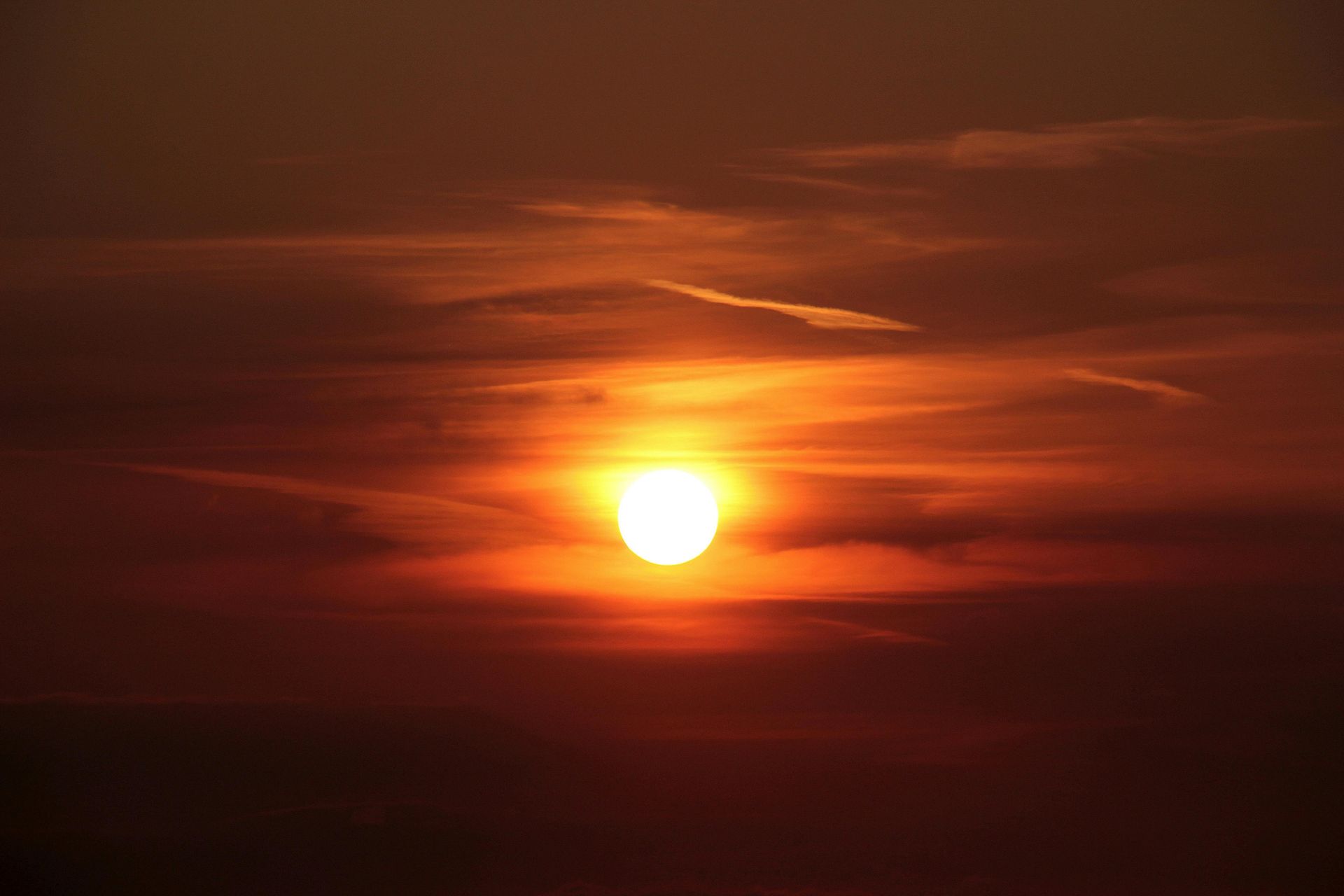 A bright, golden sun set against a backdrop of glowing orange and deep red clouds in the twilight sky.