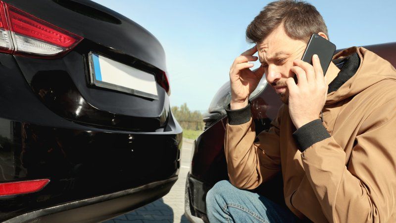 A man is talking on a cell phone next to a car that has been involved in a car accident.