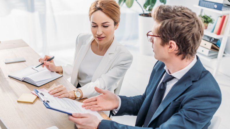 A man and a woman are sitting at a table looking at a clipboard.