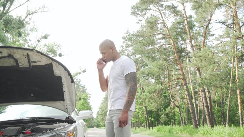 A man is talking on a cell phone next to a broken down car.