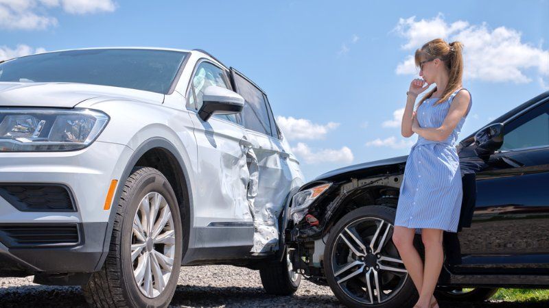 A woman is standing next to a car that has been involved in a car accident.