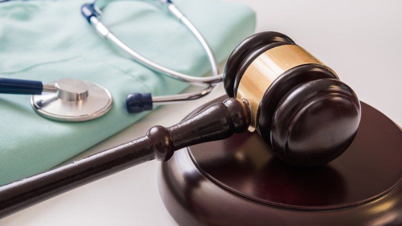 A wooden judge's gavel resting on a sounding block next to a medical stethoscope and light green surgical scrubs.