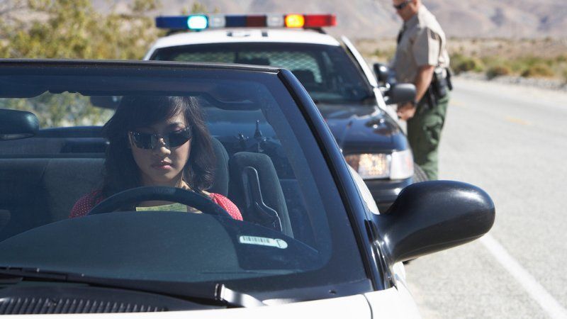 A woman is driving a car next to a police car.