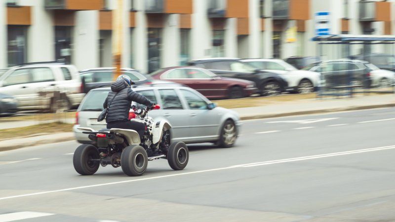 A man is riding a atv down a city street next to a car.