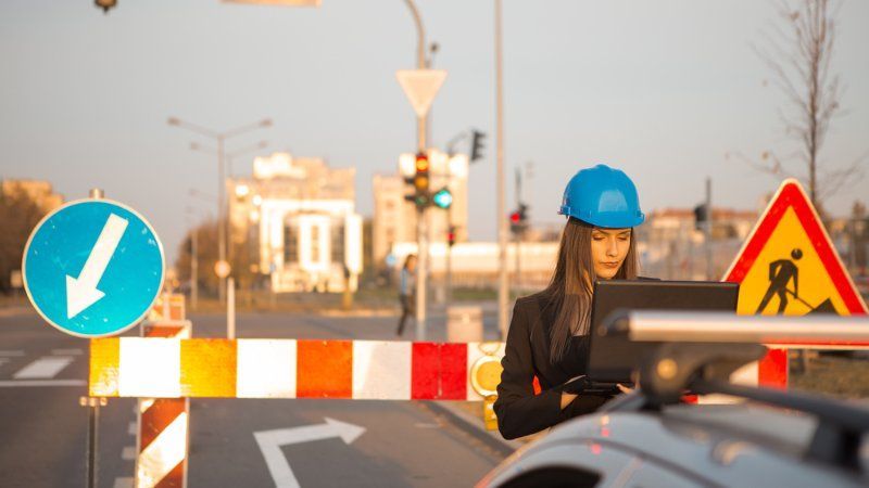A woman in a hard hat is using a laptop on a construction site.
