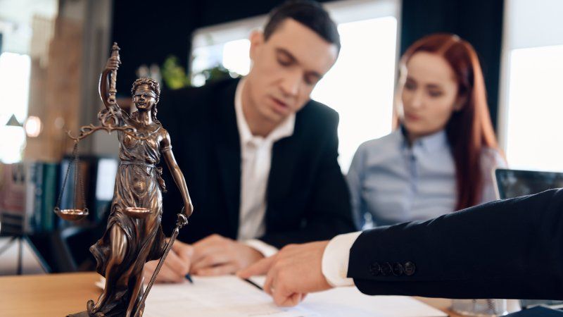 A man and a woman are sitting at a table with a statue of justice.