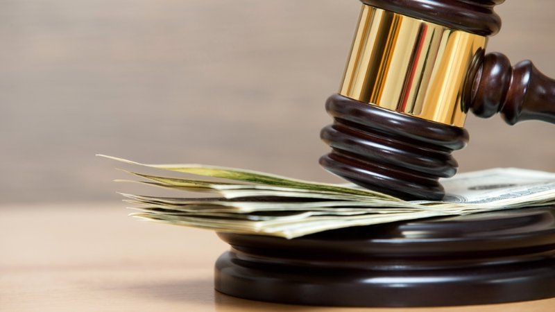 A judge 's gavel is hitting a pile of money on a wooden table.