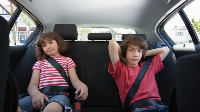 Two children wearing seatbelts sit in the back seat of a car.