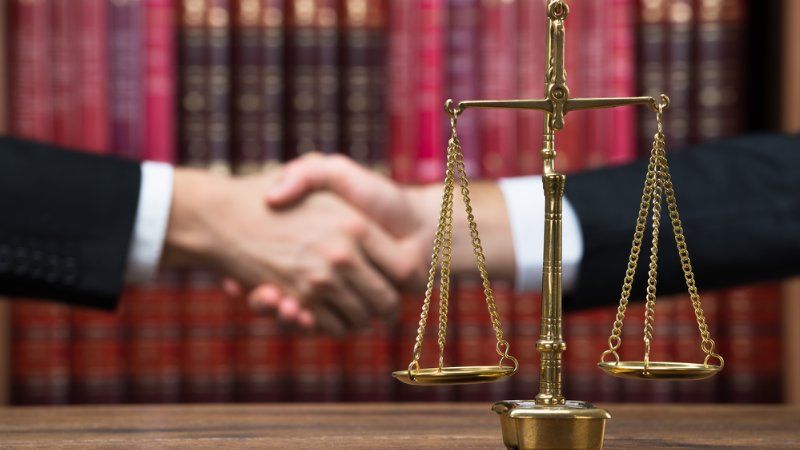 Two men are shaking hands in front of a scale of justice.