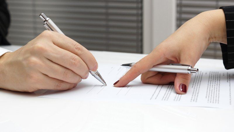 A person is writing on a piece of paper while another person points at it.
