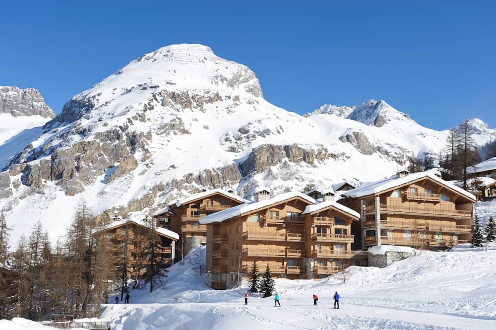 A group of people are walking in the snow in front of a snowy mountain.
