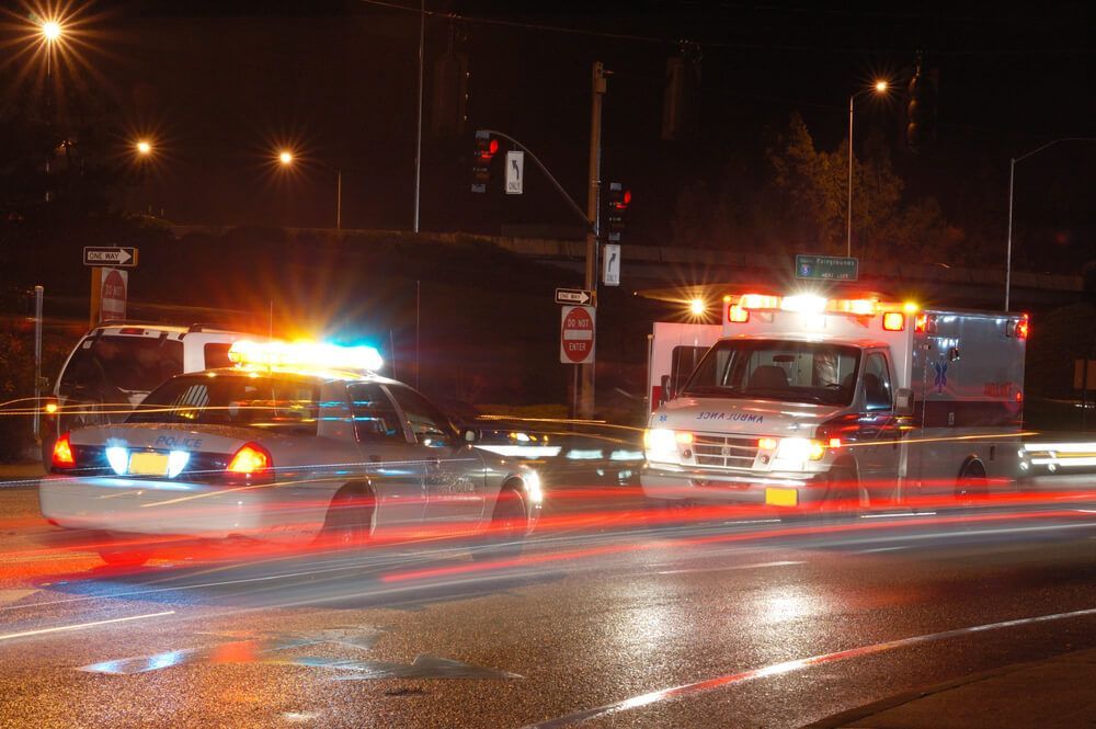 A police car and an ambulance are driving down a street at night.