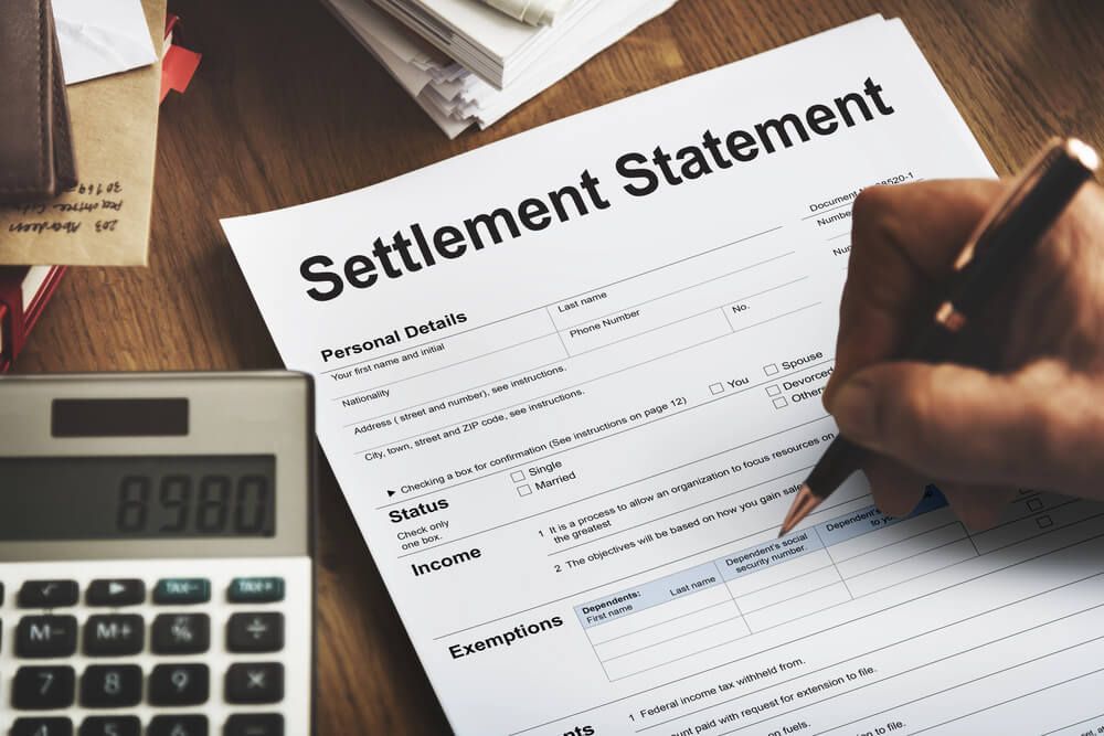A person is filling out a settlement statement next to a calculator.