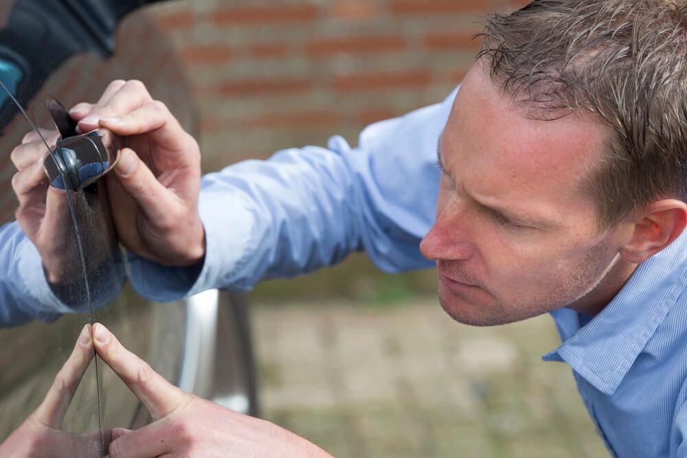 A man is looking at a scratch on the side of a car.