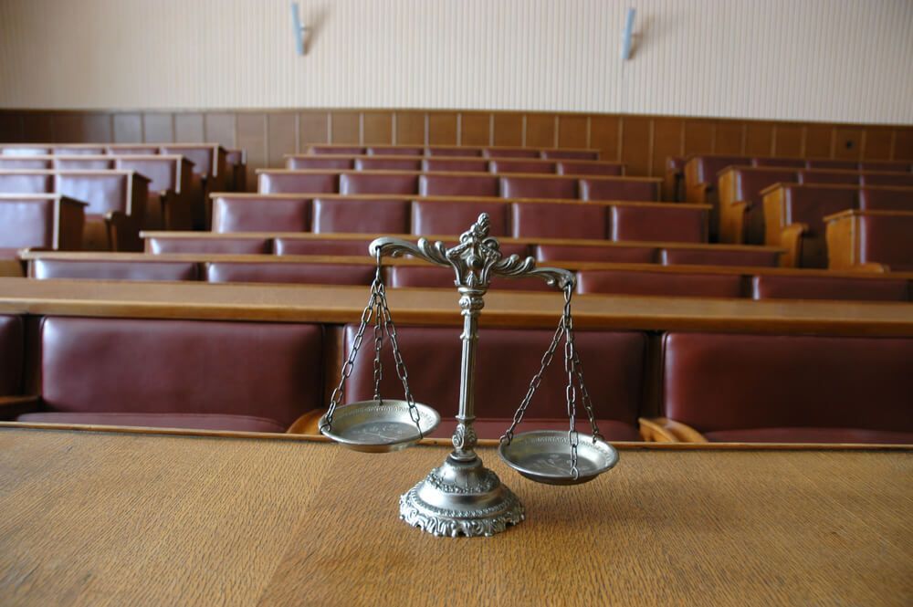 A scale of justice sits on a wooden table in a courtroom